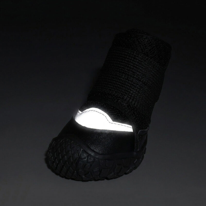 Front view of a black reflective breathable dog shoe showing the silver toe patch glowing intensely under low light.