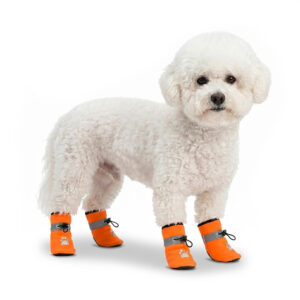 A small white Bichon Frise dog standing while wearing orange winter water-resistant fleece dog shoes with toggle cords.