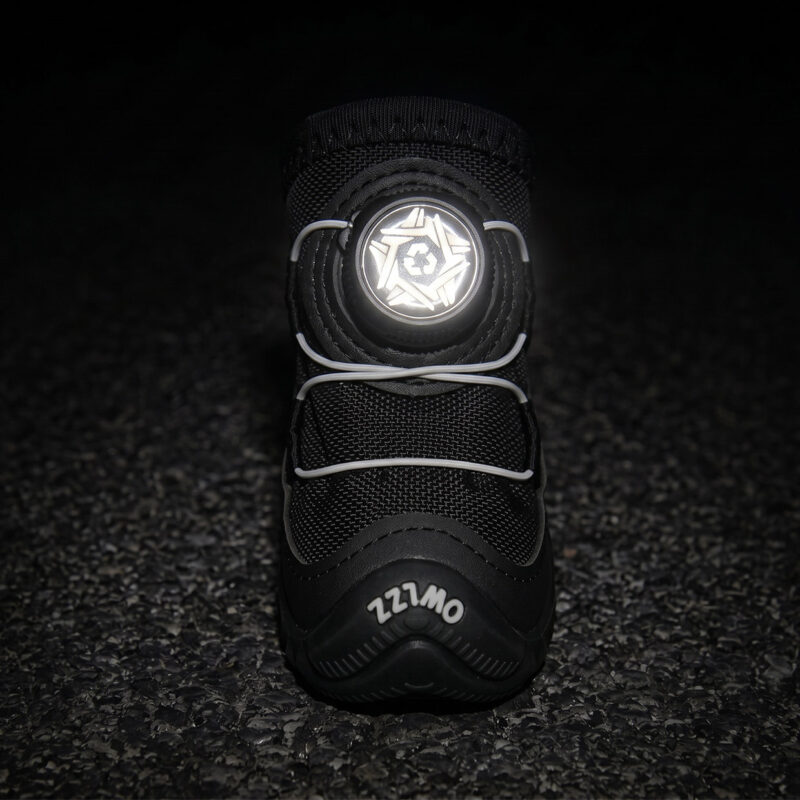 Front view of a black fleece lined dog shoe with its white central wire adjustment dial face glowing under low-light parameters.