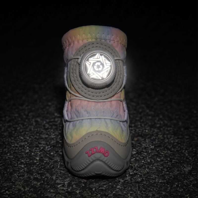 Front view of a unicorn pink dog shoe showing its central circular wire dial glowing brightly under low-light flash conditions.