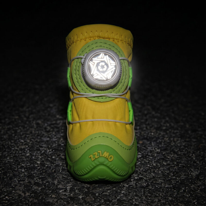 Front view of a yellow stay-on dial-system puppy shoe with its central circular wire dial face glowing brightly in darkness.