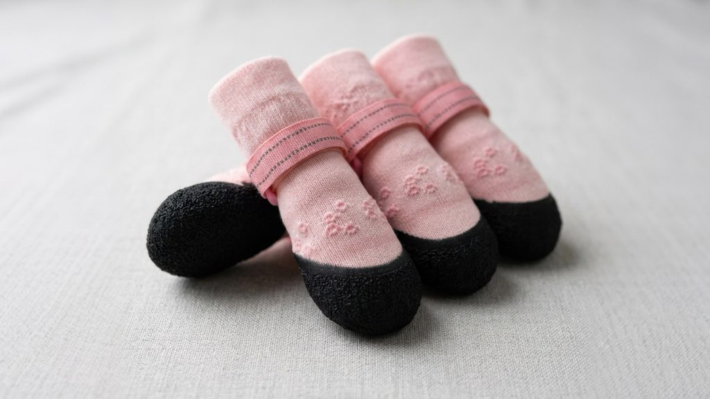 Close-up of pink knit indoor dog socks featuring textured black non-slip soles and adjustable fastening straps.